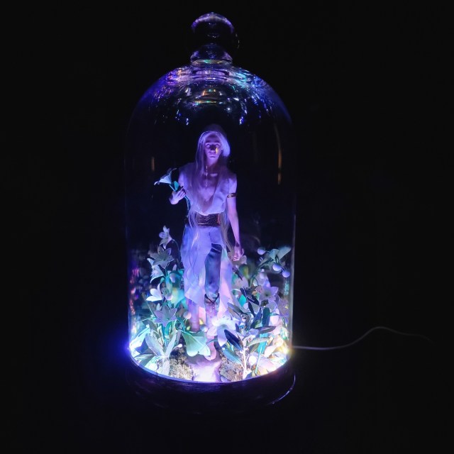 Remenaxice from Sufferborn and Elves Unwelcome as a 3d printed sculpture assembled under a glass dome with paper lilies and RGB lights.
