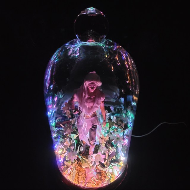 Remenaxice from Sufferborn and Elves Unwelcome as a 3d printed sculpture assembled under a glass dome with paper lilies and RGB lights.